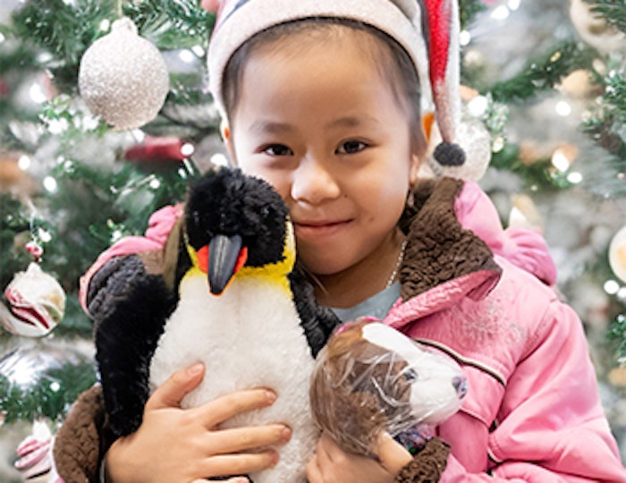 a smiling little girl cuddles a stuffed penguin and a stuffed dog