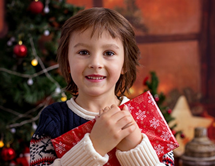 a young girl smiling and holding a wrapped christmas present